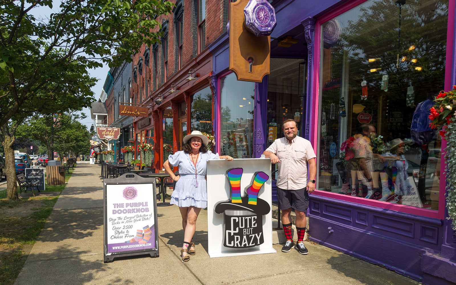 Rachel Northrup McGee and Scotty McGee hold the 'Cute But Crazy' sock store sign while standing in front of The Purple Doorknob sock shop in Ellicottville, New York.