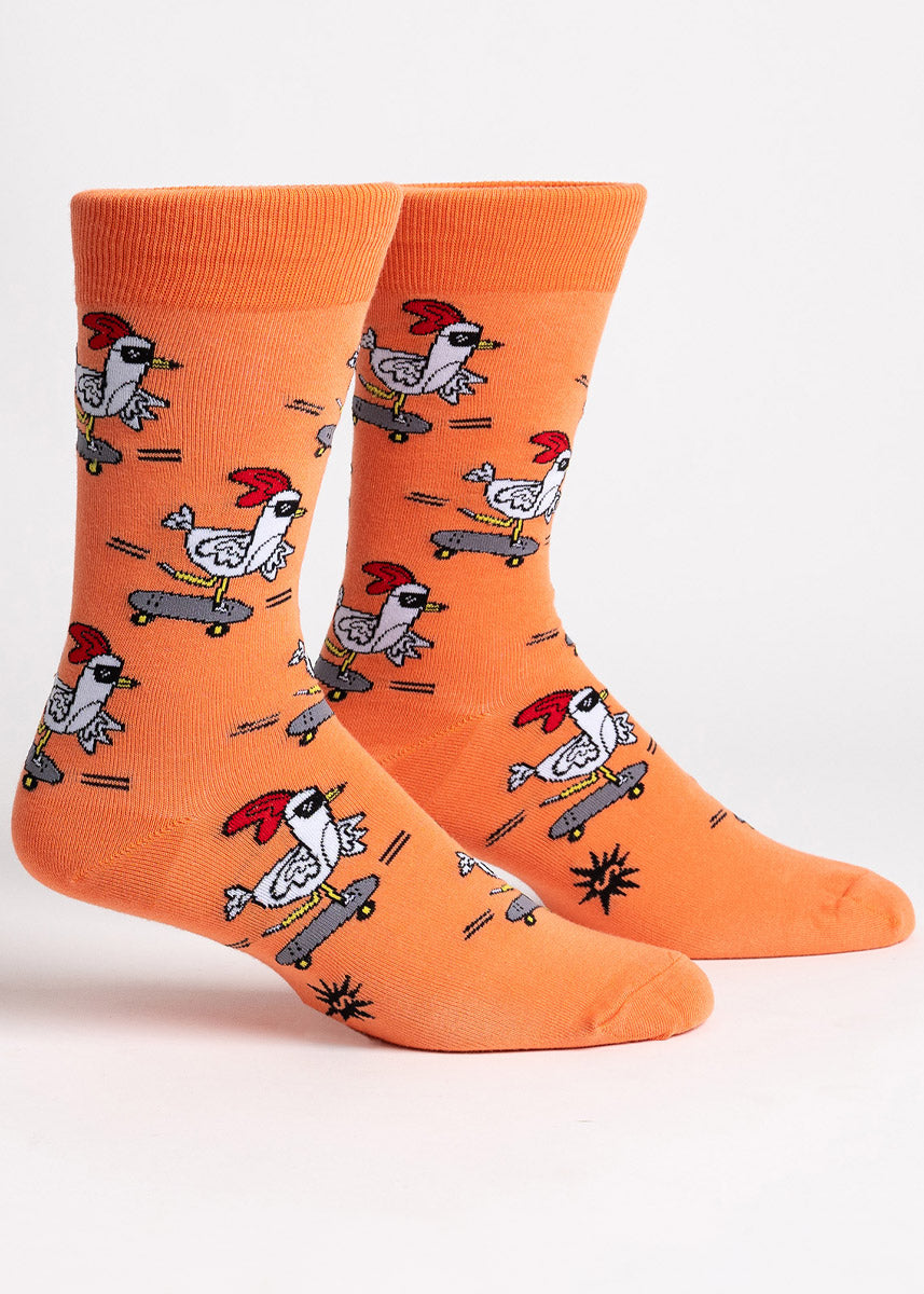 Orange crew socks for men feature an allover pattern of white chickens wearing sunglasses and riding skateboards.