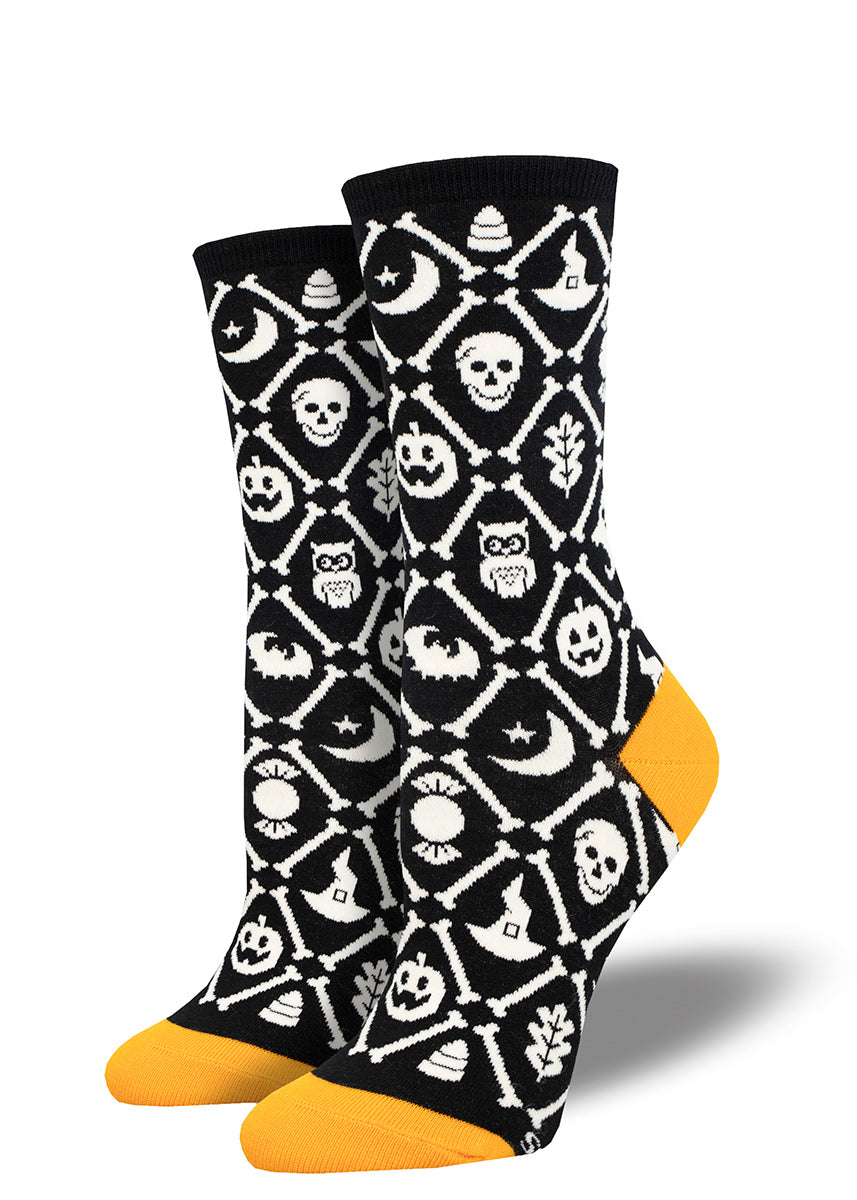Black and white women's crew socks with orange accents feature a repeating pattern of Halloween icons arranged within a diamond pattern bordered with bones.