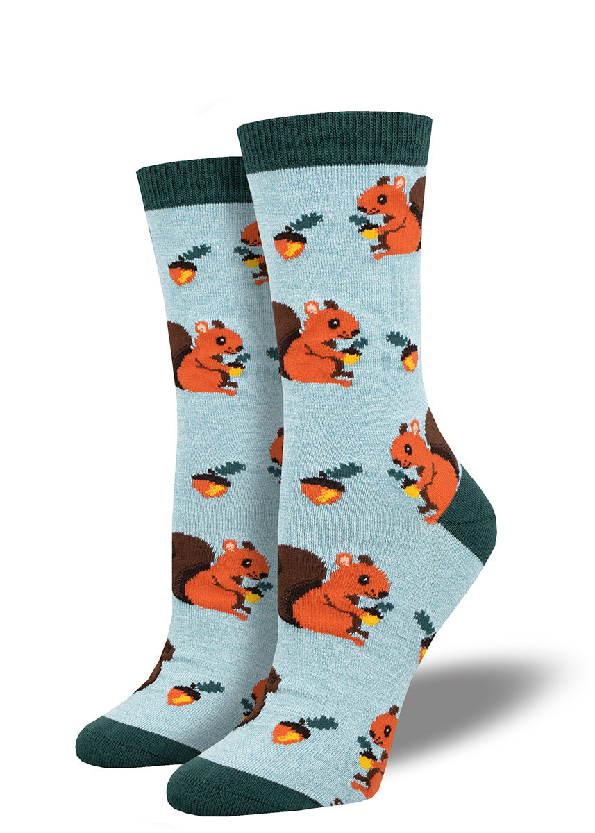 Light blue crew socks for women with a dark teal band, toe, and heel and a repeating pattern of acorns and red squirrels holding acorns.