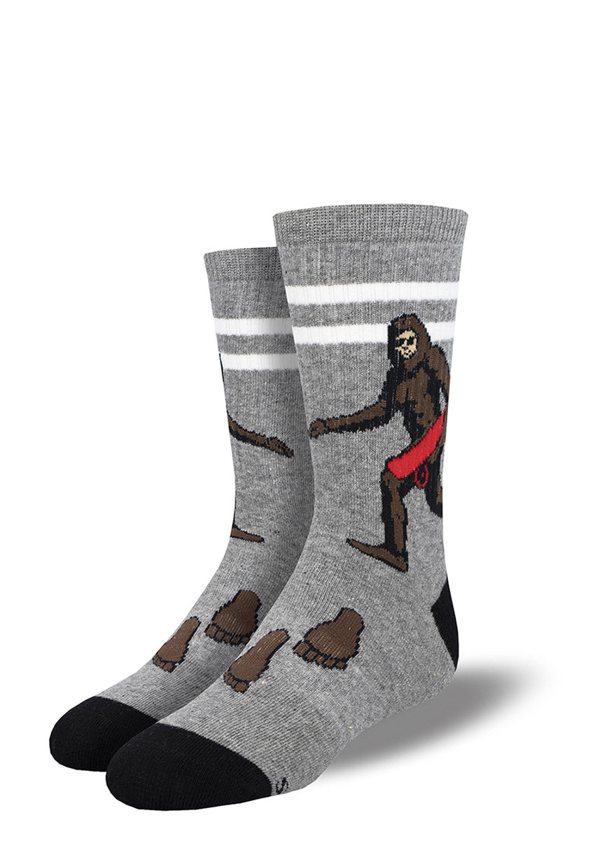 Heather gray athletic socks for kids decorated with an image of Sasquatch carrying a red skateboard, along with footprint embellishments.