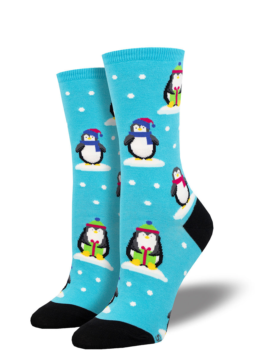 Blue crew socks for women show penguins posing with presents in the snow while wearing winter hats and scarves.