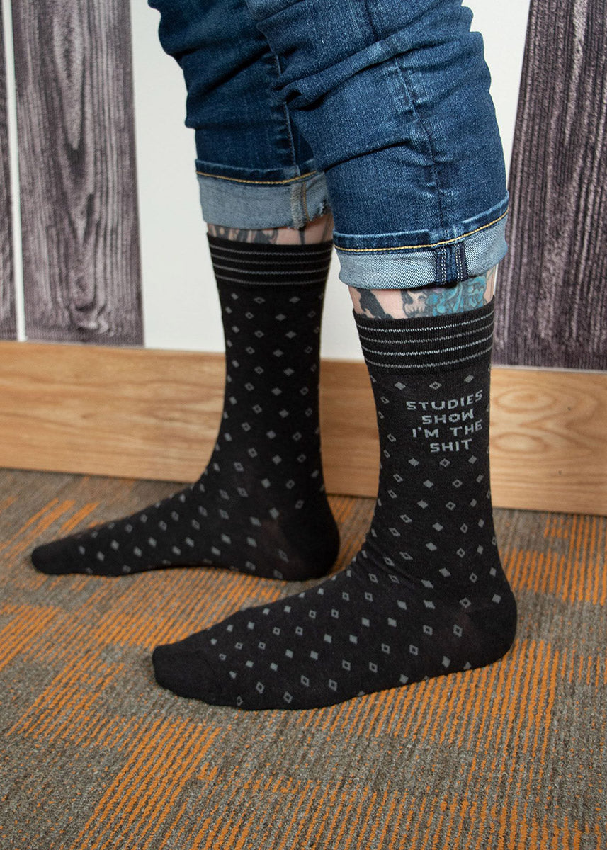 A model wearing novelty socks that read &quot;Studies Show I&#39;m The Shit&quot; and cuffed jeans poses indoors. 