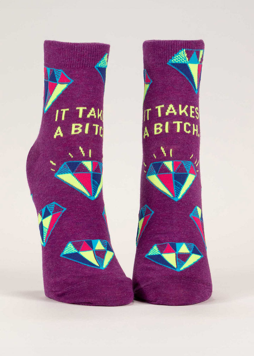 Vibrant plum ankle socks with a colorful repeating hand-drawn diamond pattern and the words “It Takes a Bitch”  in yellow.