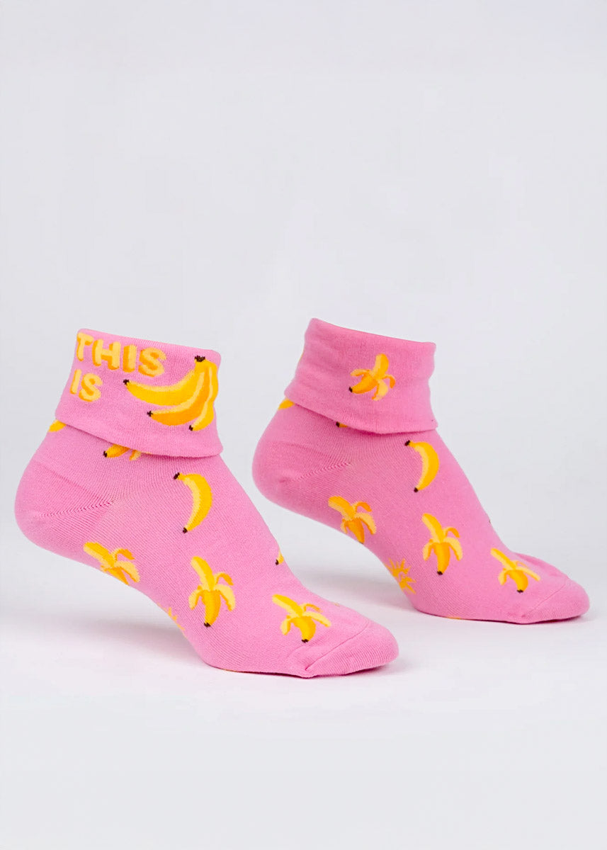 Pink turn-cuff ankle socks with an allover pattern of yellow bananas that say "This Is" followed by a bunch of bananas on the cuff.