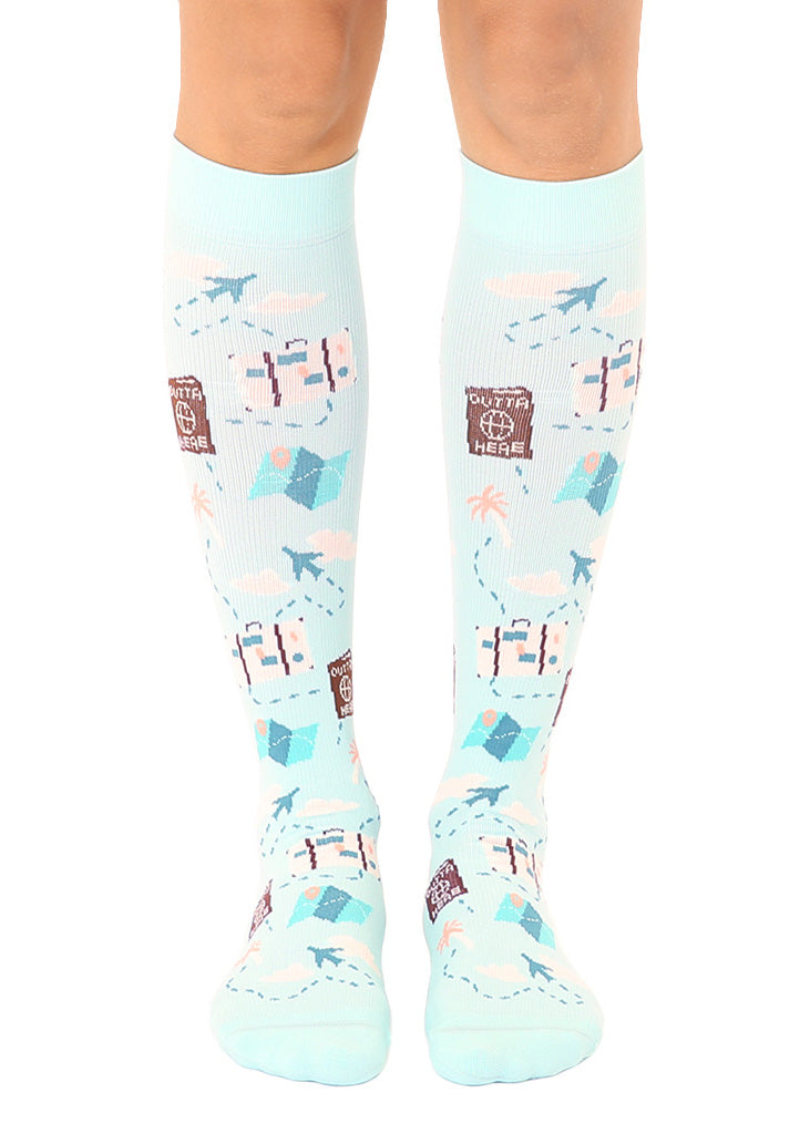 Knee-high compression socks with an allover pattern in a travel theme including airplanes, luggage, maps and more against a light blue sky background.