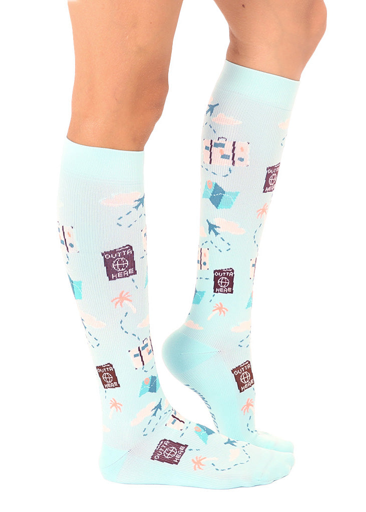 Knee-high compression socks with an allover pattern in a travel theme including airplanes, luggage, maps and more against a light blue sky background.