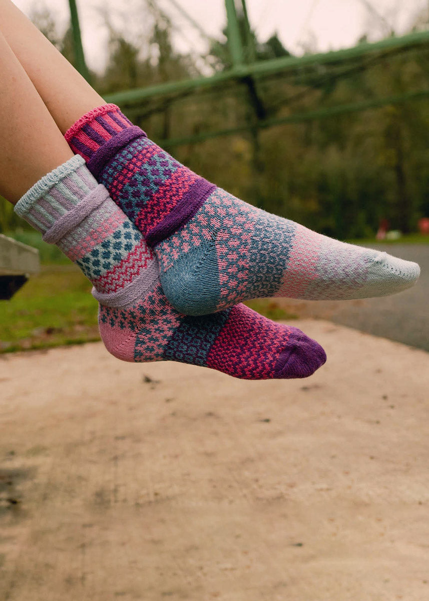 Intentionally mismatched crew socks with different sections featuring various geometric patterns like stripes and dots in shades of blue, aqua, purple and pink.