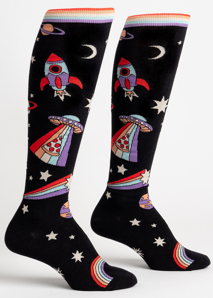Black space-themed knee-high socks feature stars, planets, rainbows, spaceships and a UFO beaming up a slice of pizza. 