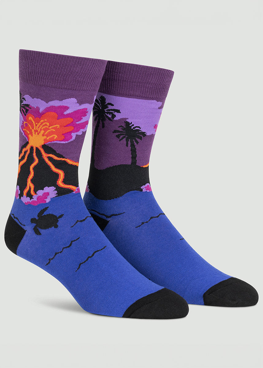 Blue and purple men&#39;s crew socks with a design featuring a volcanic island at night with palm trees, red and orange lava and sea turtles swimming in the ocean below.