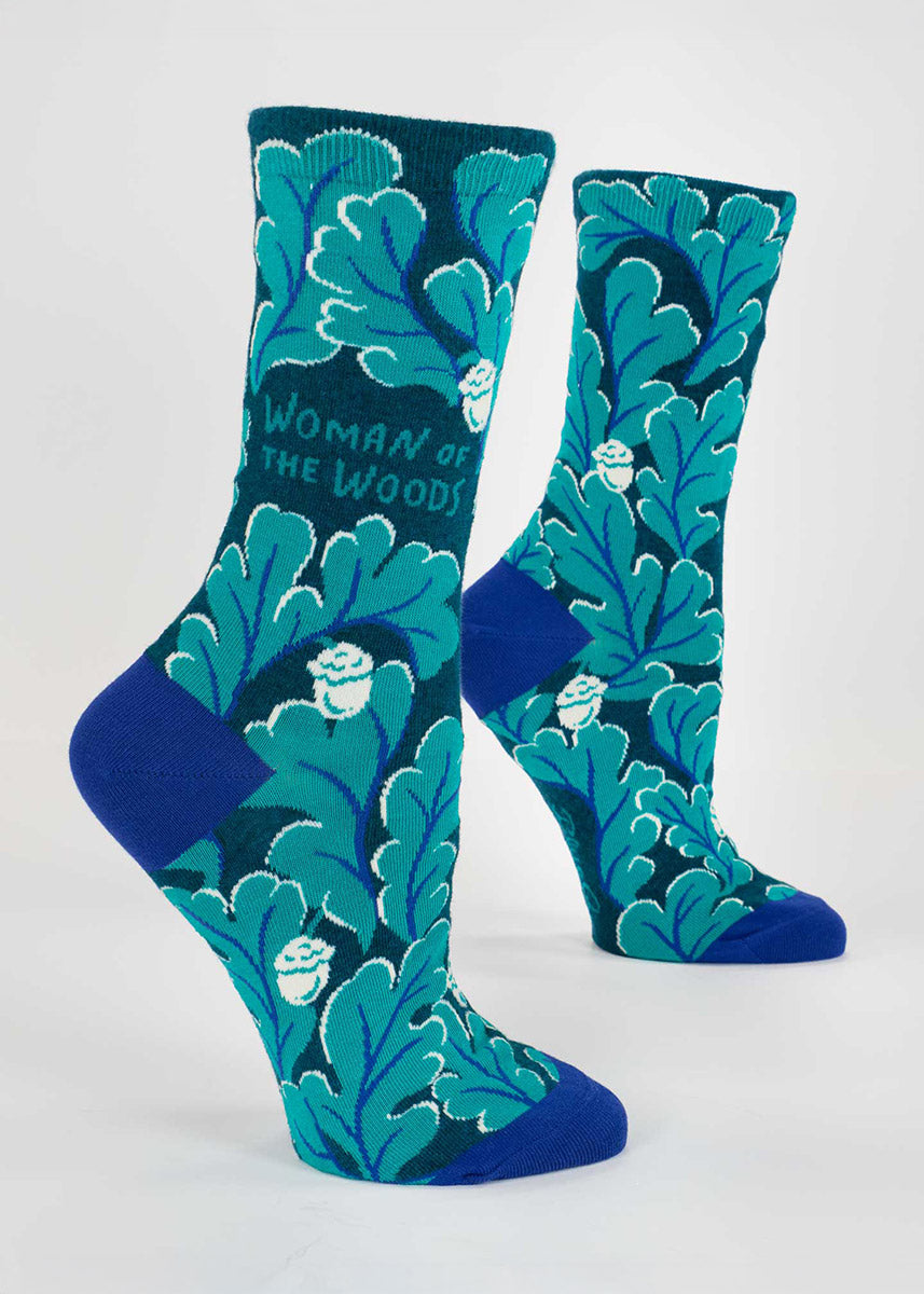 Teal socks with an acorn and oak leaf pattern that say "Woman of the Woods" on the cuff.