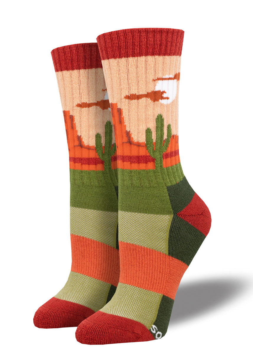 Red, orange, and green wool hiking socks for women feature a desert landscape scene with cacti and sandy dunes.