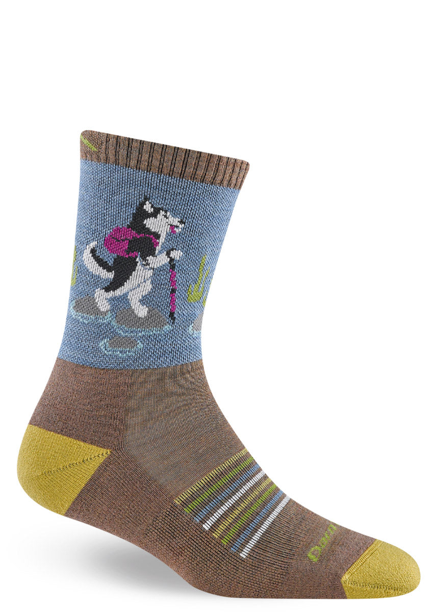 Blue and brown wool hiking crew socks for women that feature a black and white husky standing on its hind legs and hiking while wearing a backpack and holding a walking stick.
