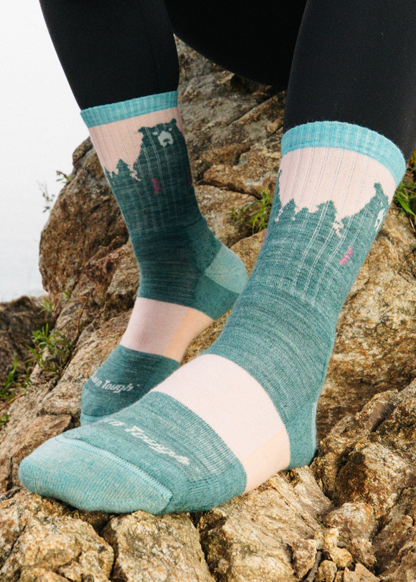 Teal and pale pink wool hiking socks for women featuring a bear design against a forest background.