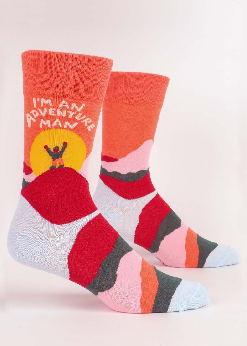 Funny socks for men show a triumphant figure on top of a colorful mountain with the words, "I'm an adventure man!"
