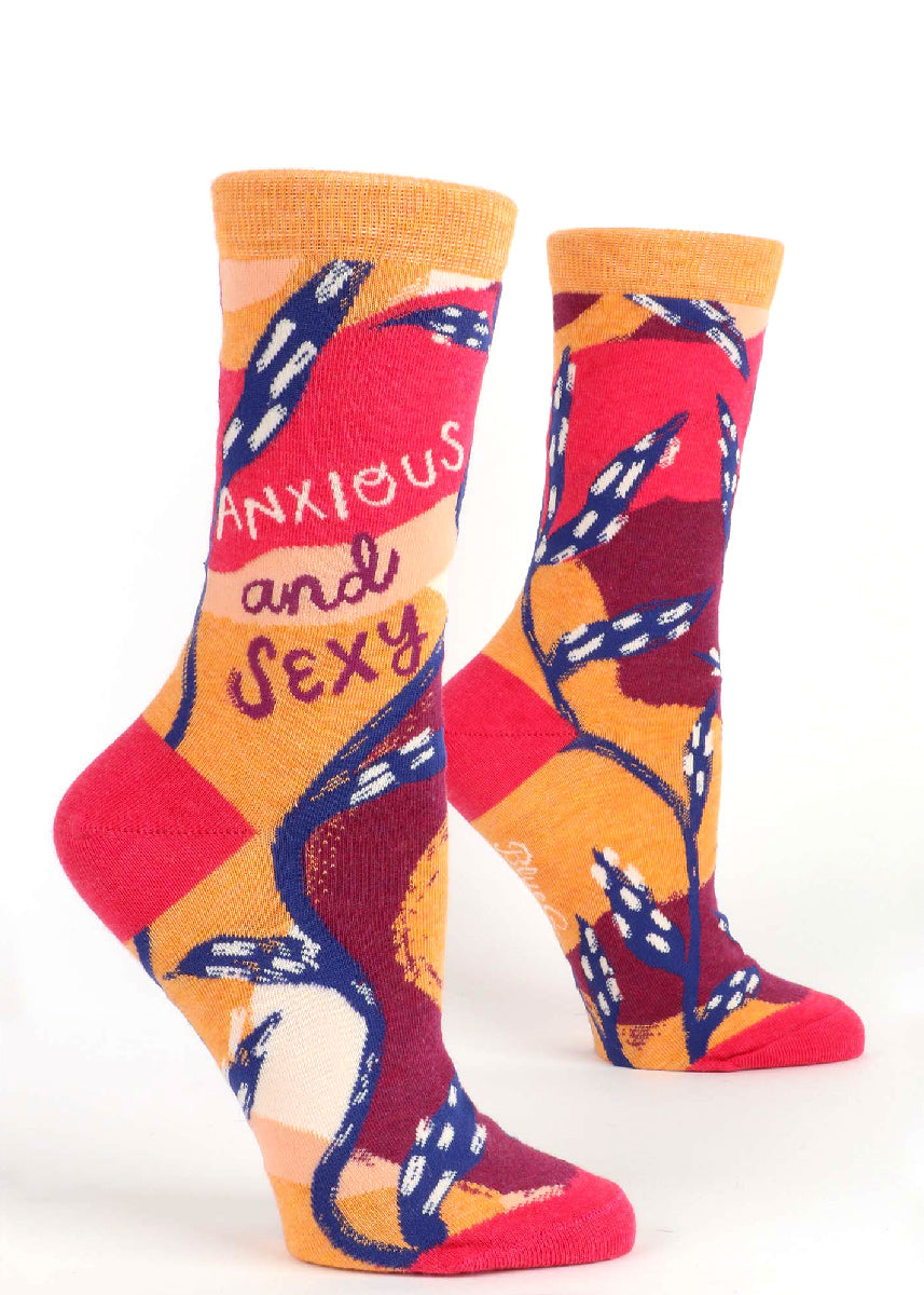 Funny socks for women say "Anxious and Sexy" over a bold abstract background of red, orange, burgundy, and dark blue.
