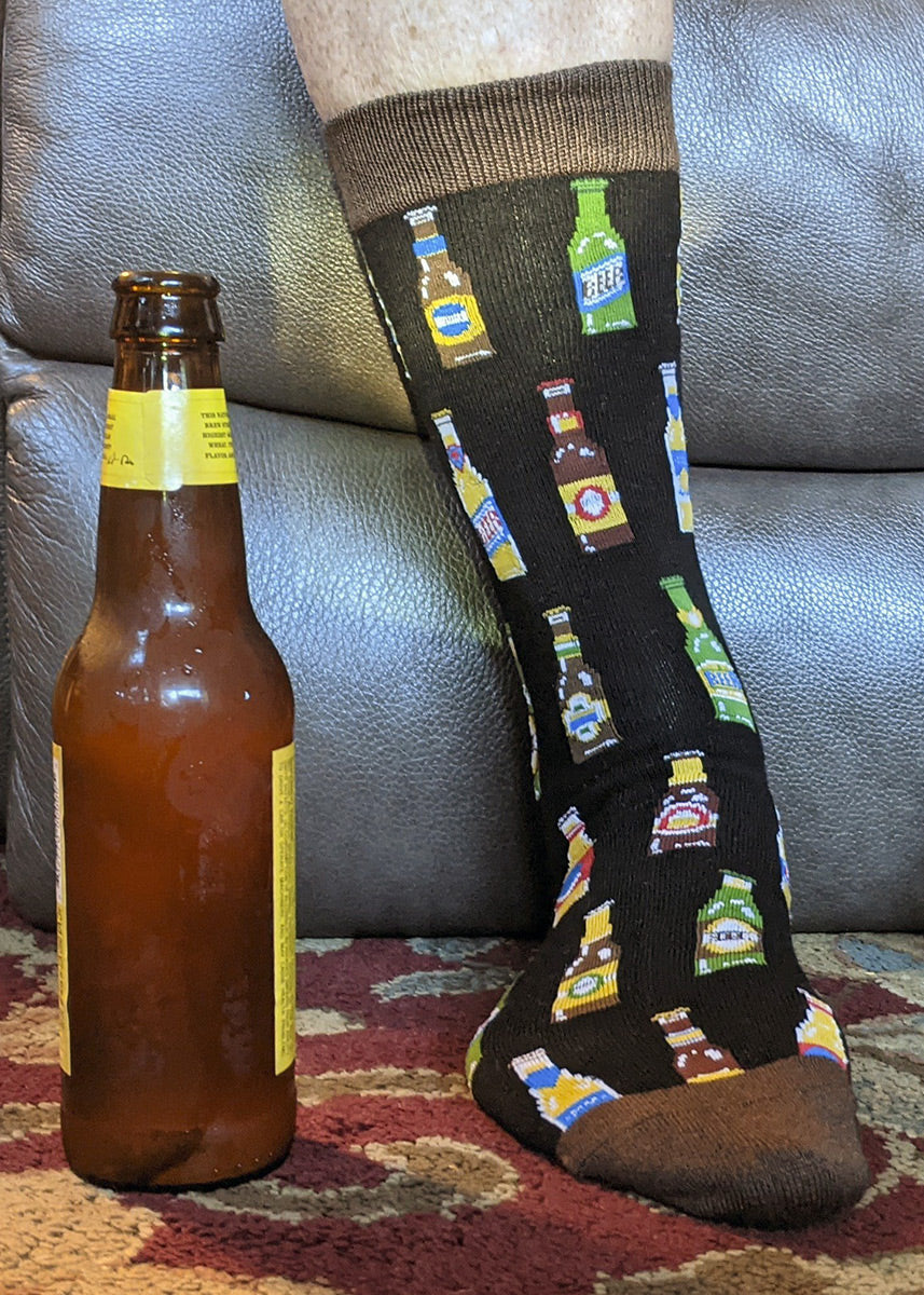 Dad wears a bamboo sock featuring a pattern of various beer bottles, posed next to an actual bottle of beer for size reference.