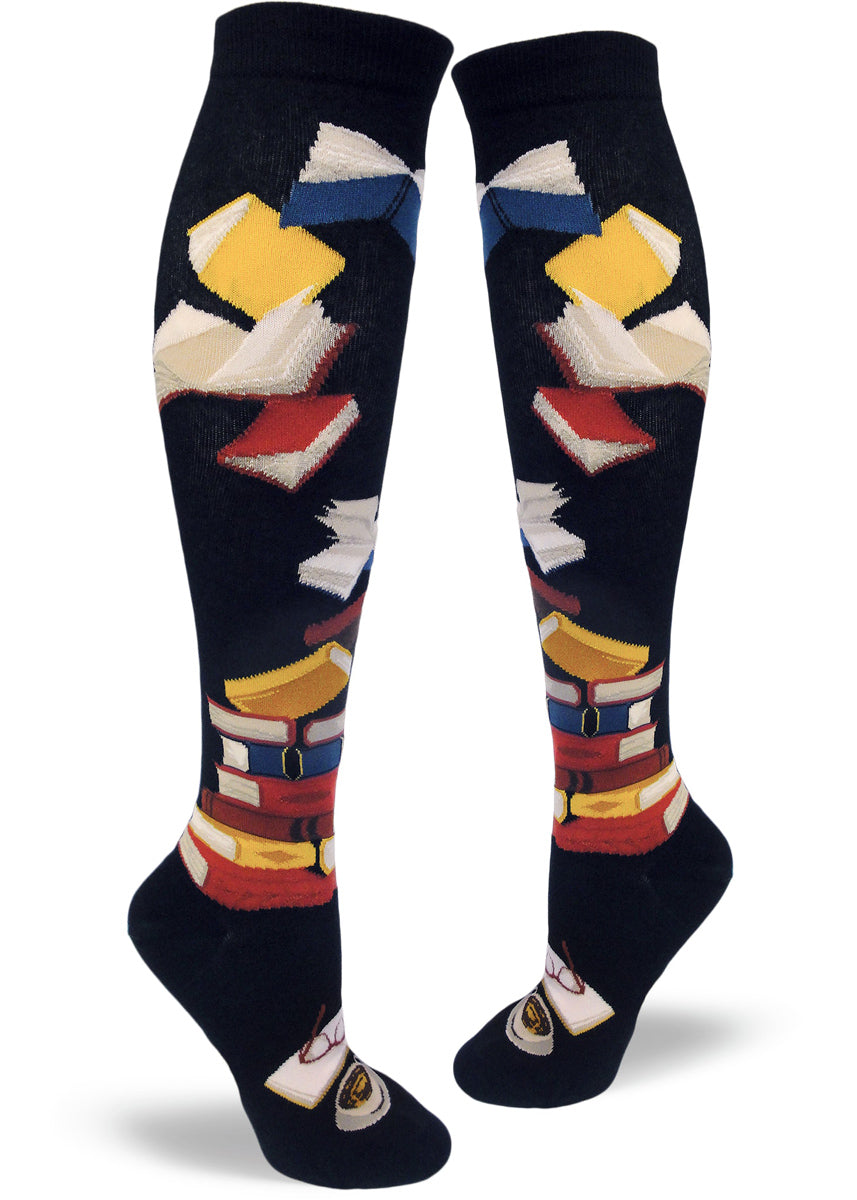 Knee-high book socks for women with stacks of books, flying books and a book being read on a black background