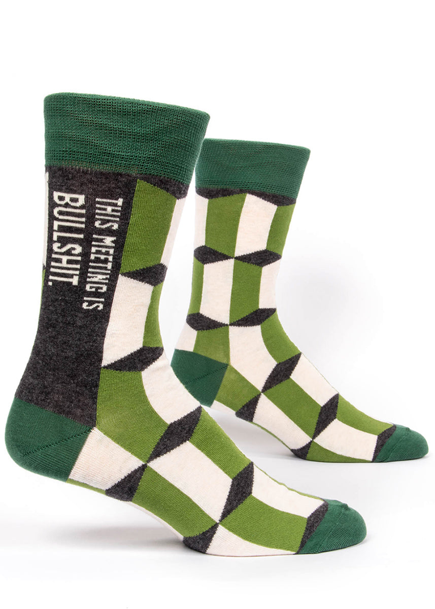 Funny swear word men's socks that say "This Meeting is Bullshit" on a green patterned background.