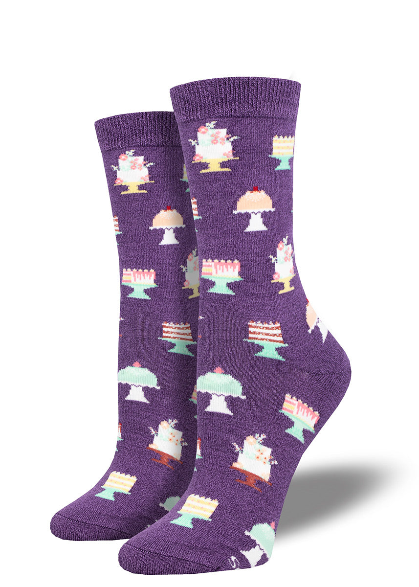 Purple bamboo crew socks feature a pattern of different kinds of cake including layer cakes for birthdays and weddings, each displayed on a cake plate.