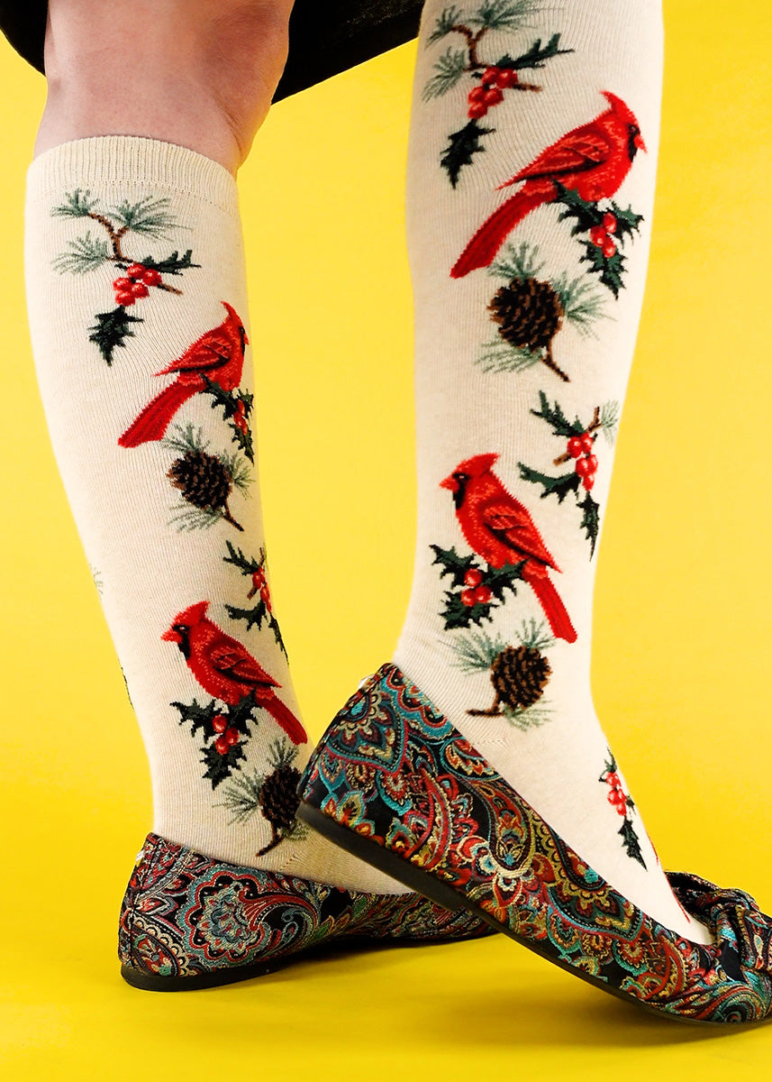 Cute knee high socks for Christmas feature red cardinals with winter greenery on a taupe background.