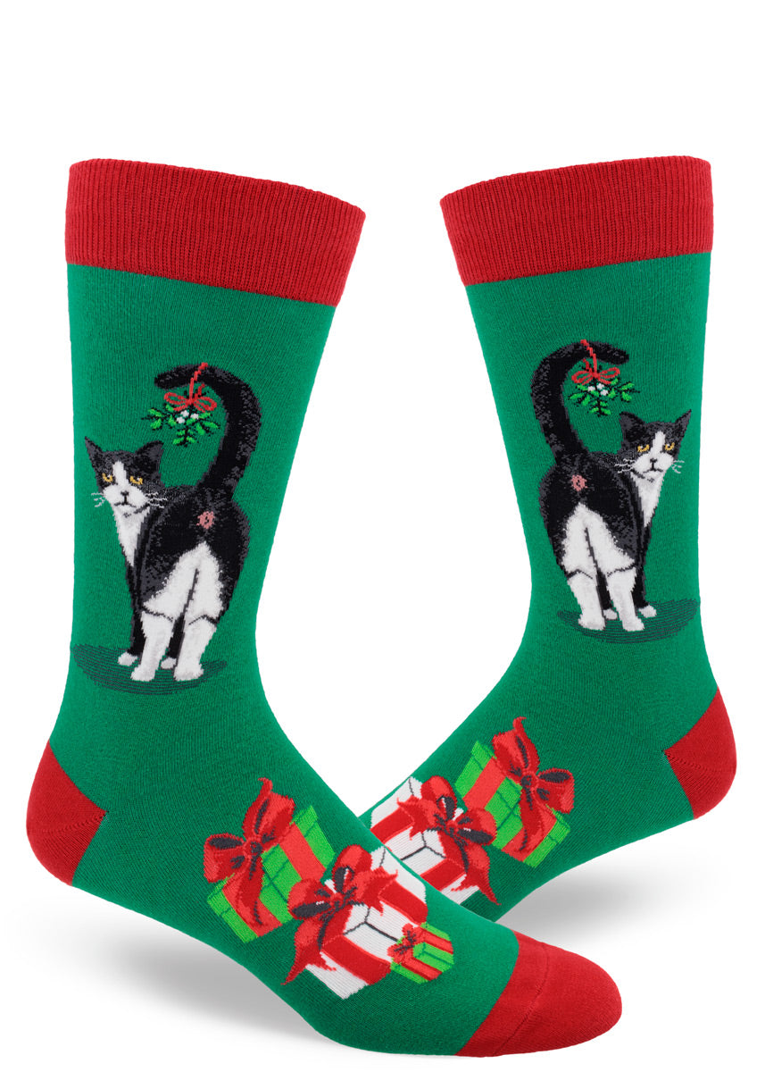 Green men&#39;s crew-length Christmas socks with red accents depict Tuxedo cats showing off their behind with a sprig of mistletoe hanging from their tail, giving a cheeky look from over their shoulder.