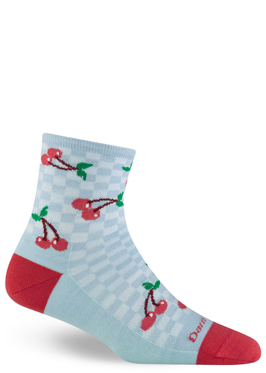 Aqua ankle socks for women with red accents have a checkerboard background behind a pattern of bright red cherries.