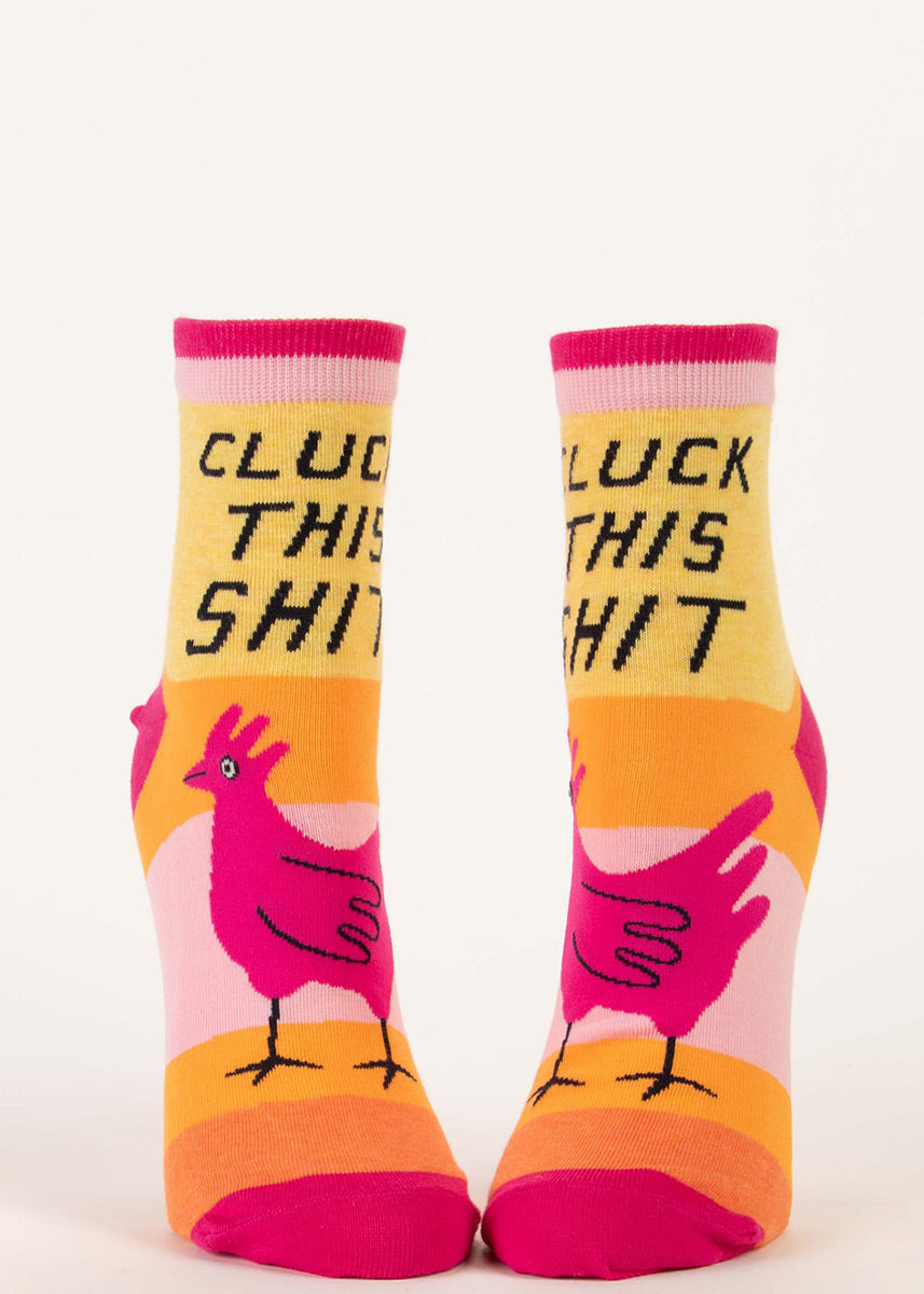 Funny ankle socks feature pink chickens and say “Cluck This Shit” on a striped pink, yellow and orange background.