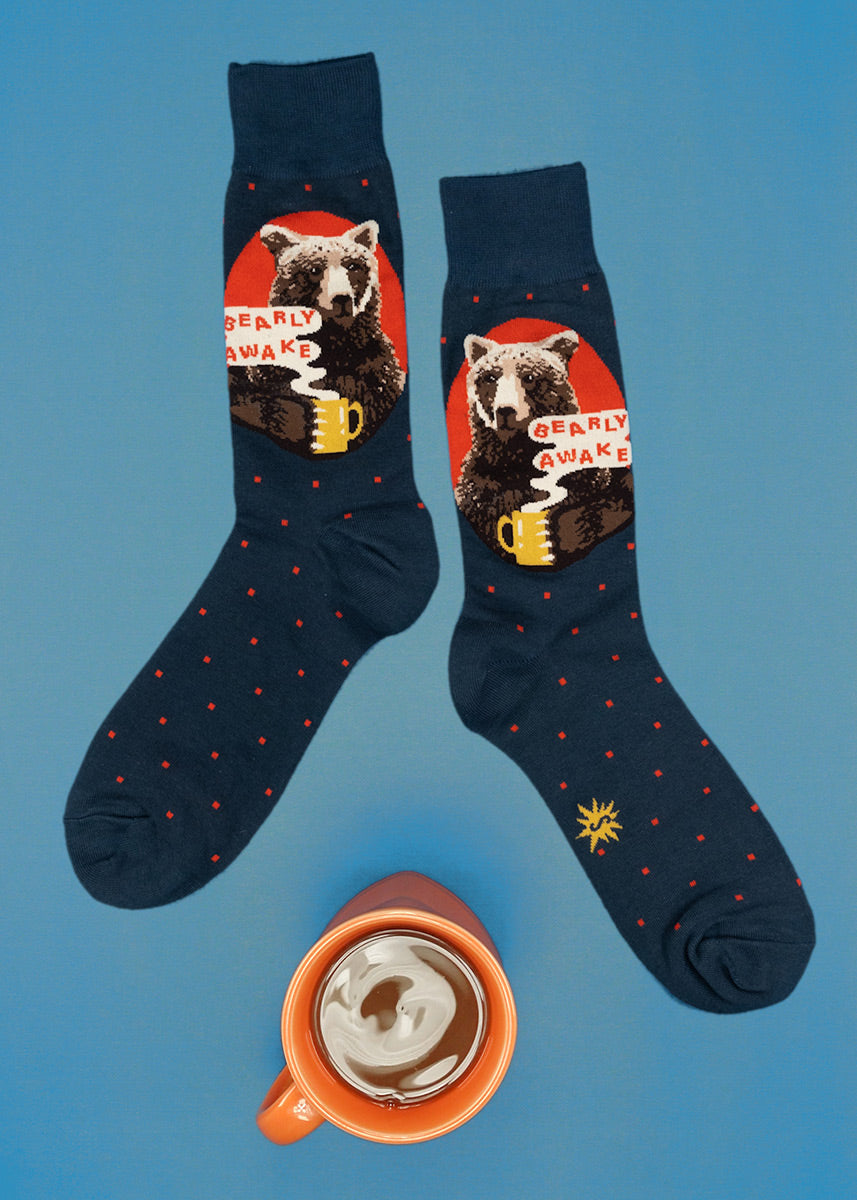 Funny crew socks for men show a grizzly bear with a mug of coffee and the words, "Bearly Awake."