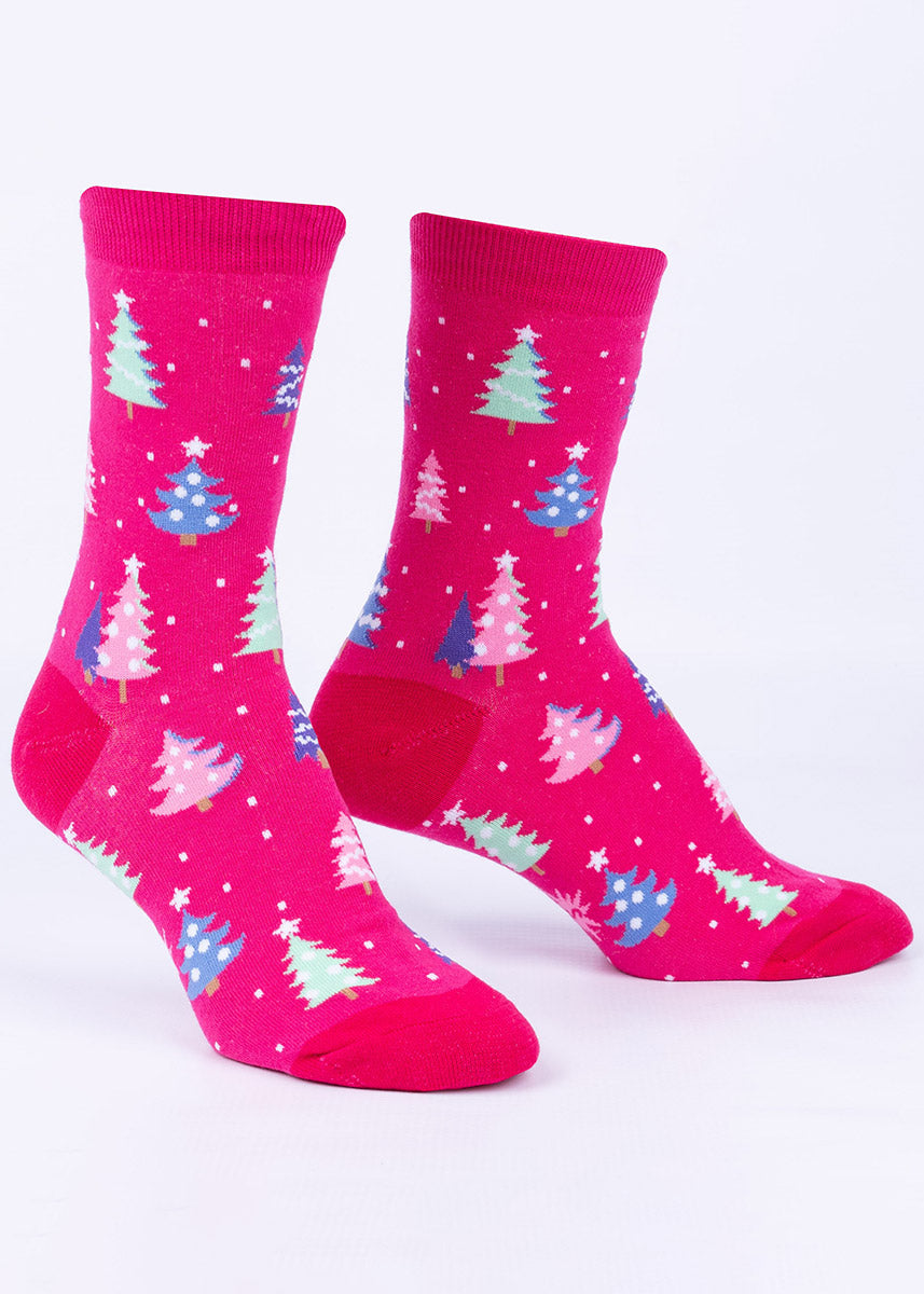 Glow-in-the-dark Christmas socks depict snow falling on multicolored Christmas trees in pink, blue and green over a bright pink background.