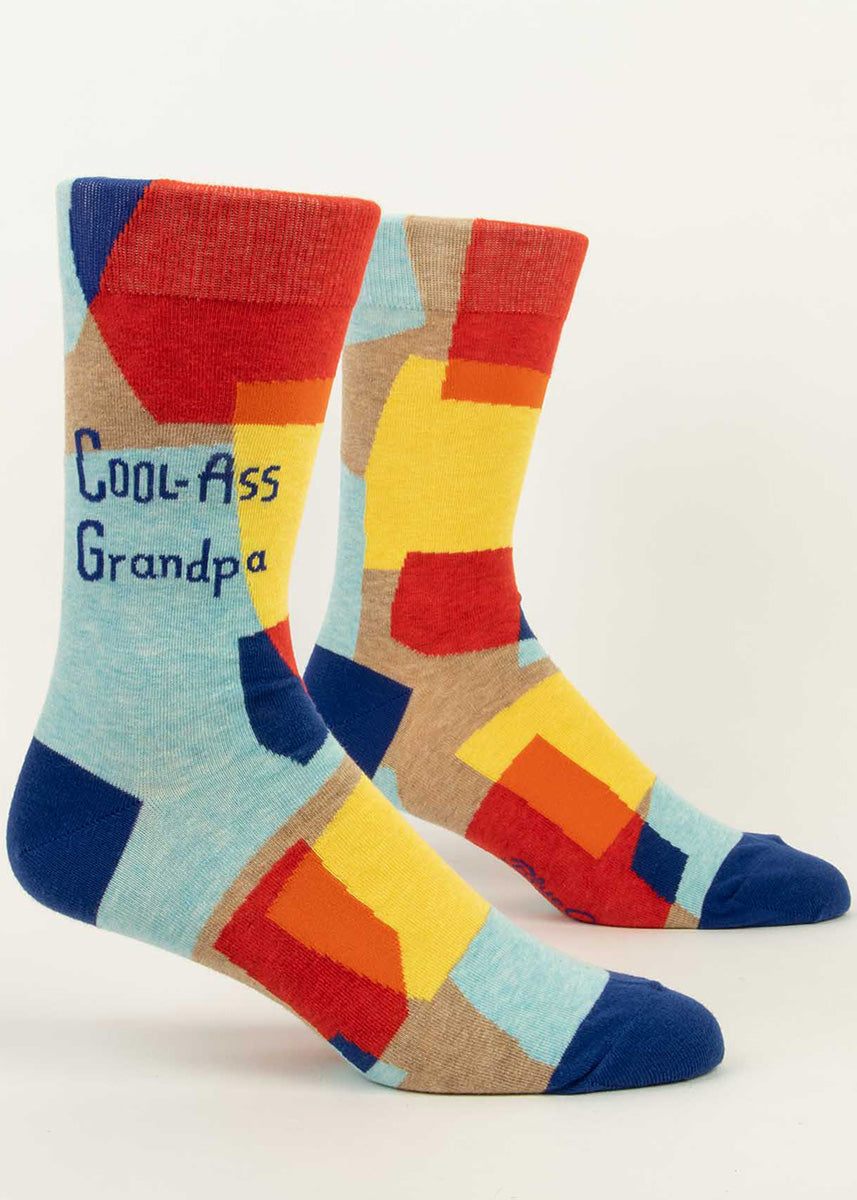 Funny crew socks for men feature yellow, red, and blue shapes on a taupe background with the words, "Cool-Ass Grandpa."