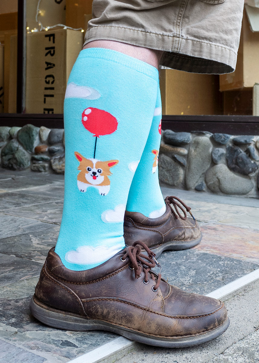 A model wears a pair of sky blue socks, with a corgi tied to a balloon floating in the clouds.