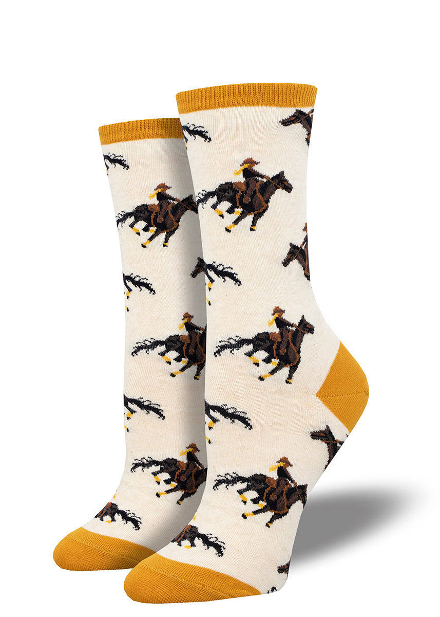 Novelty crew socks for women with a repeating pattern of female riders on the backs of bay horses against a light cream background.