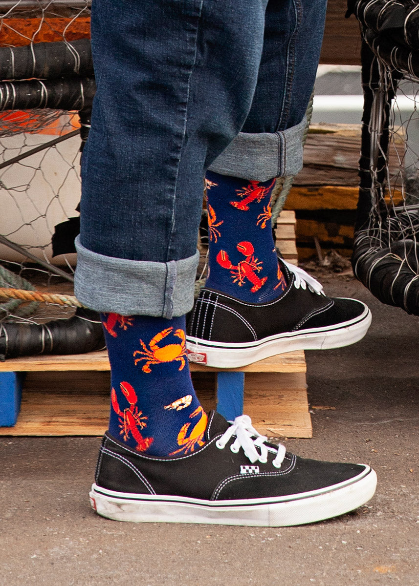 A man wears a pair of navy blue socks with crabs, lobsters and other crustaceans on them.