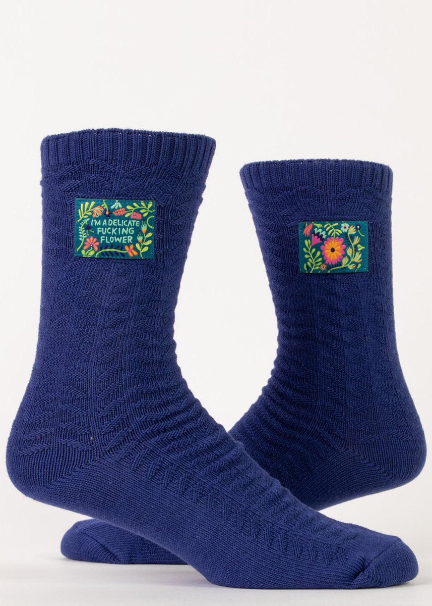 Funny swear word socks feature floral tags that say &quot;I&#39;m a delicate fucking flower&quot; on a dark blue knit background.