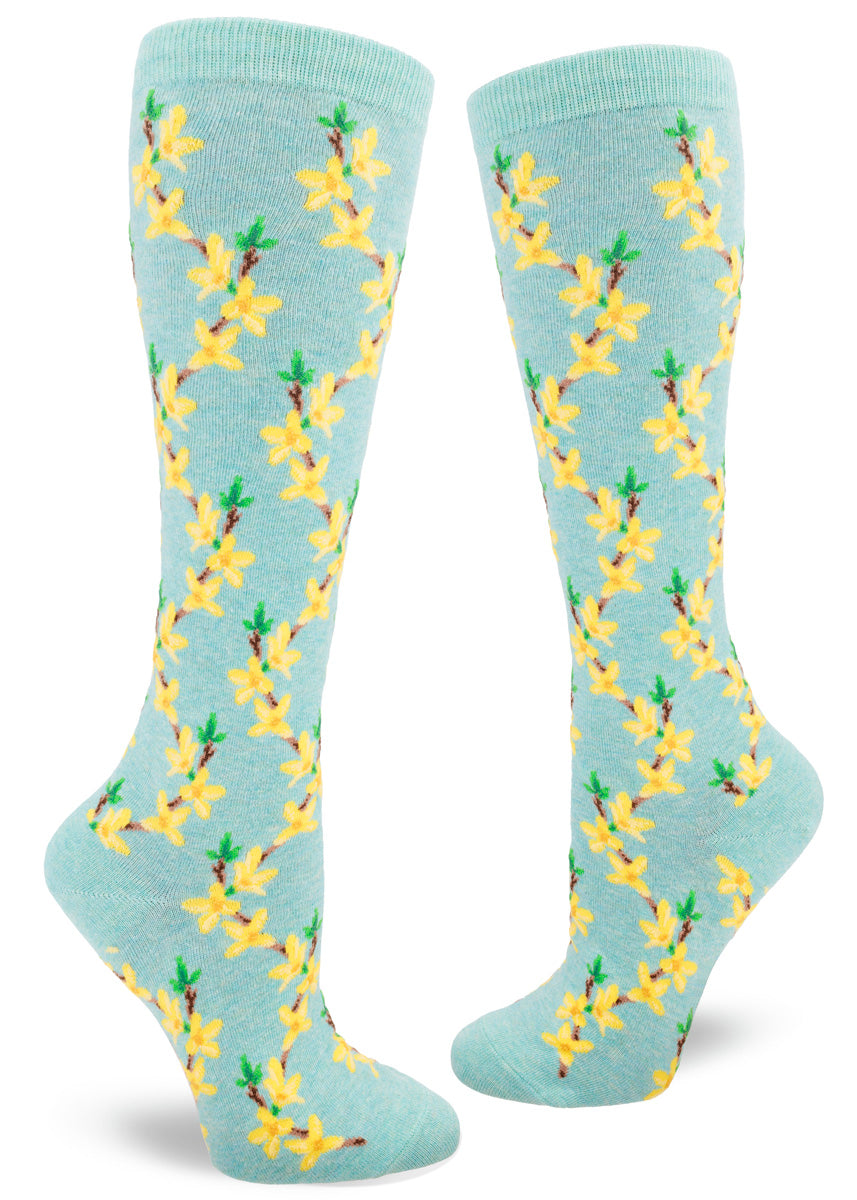 Floral knee-high socks feature a repeating pattern of forsythia flowers, the yellow buds arranged along brown branches, over a pale aqua heather background.