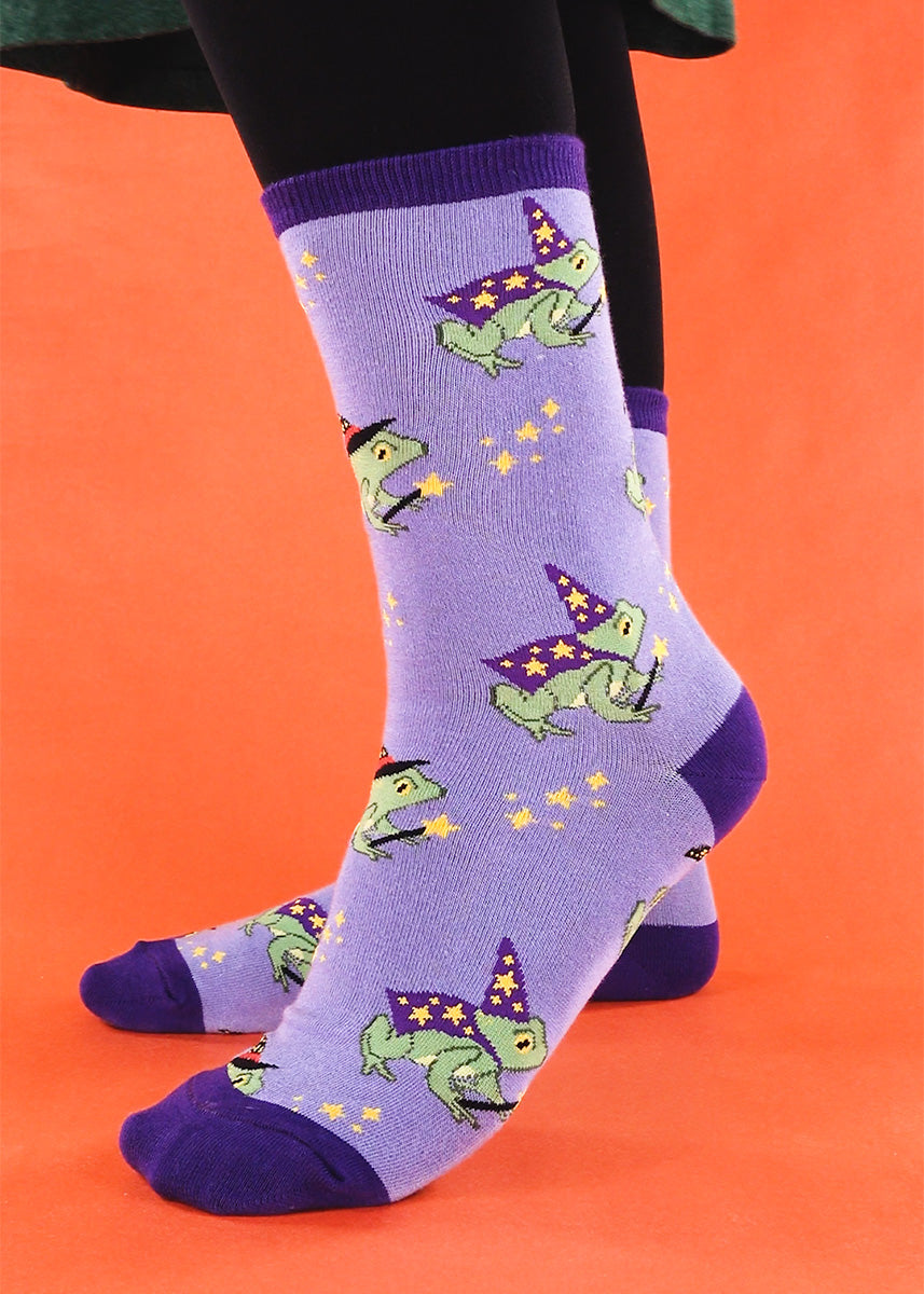 Funny frog socks for women show frogs wearing capes and witch and wizard hats and pointing their magic star wands. 