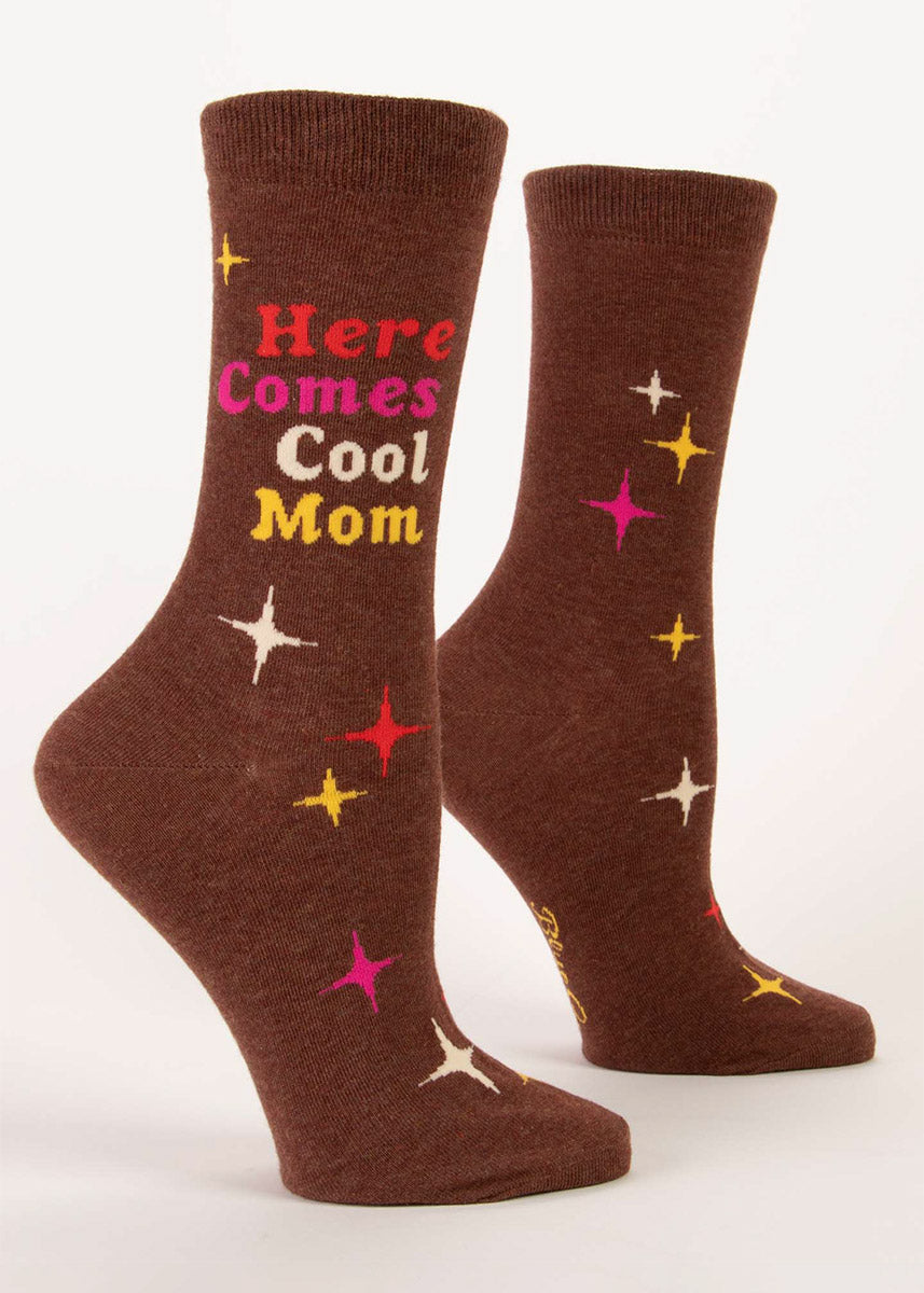Brown crew socks that say “Here Comes Cool Mom” in colorful retro lettering surrounded by an embellishment of four-pointed atomic stars.