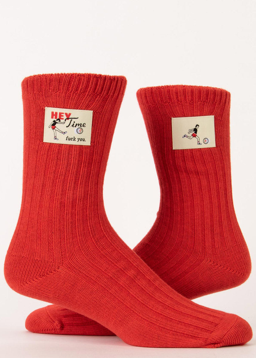 Funny swear word socks feature tags that say "Hey time, fuck you" and a person kicking a clock on a red knit background!