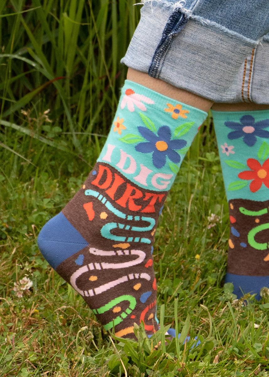 A model wearing garden-themed novelty socks that read &quot;I Dig Dirt&quot; poses in the grass.