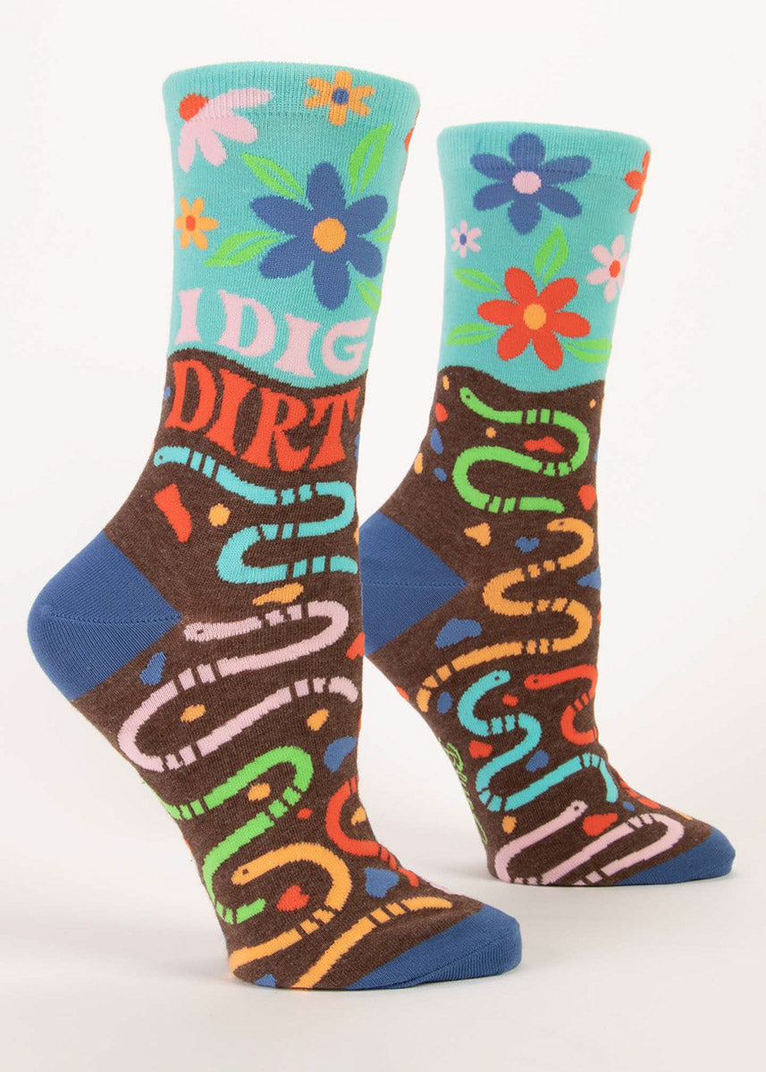 Women's crew socks in sky blue and brown with earthworms and flowers in rainbow colors and the words “I DIG DIRT.”  