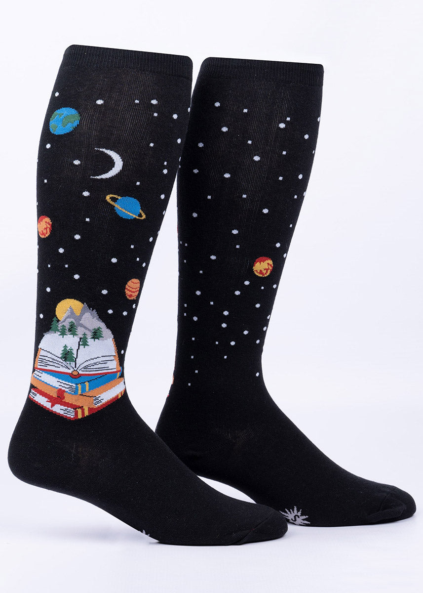 Black knee socks with a design featuring a stack of books opening to reveal trees, mountains, stars and planets.