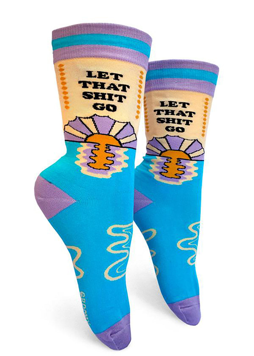Funny socks for women say "Let that shit go" over a sun setting above water.