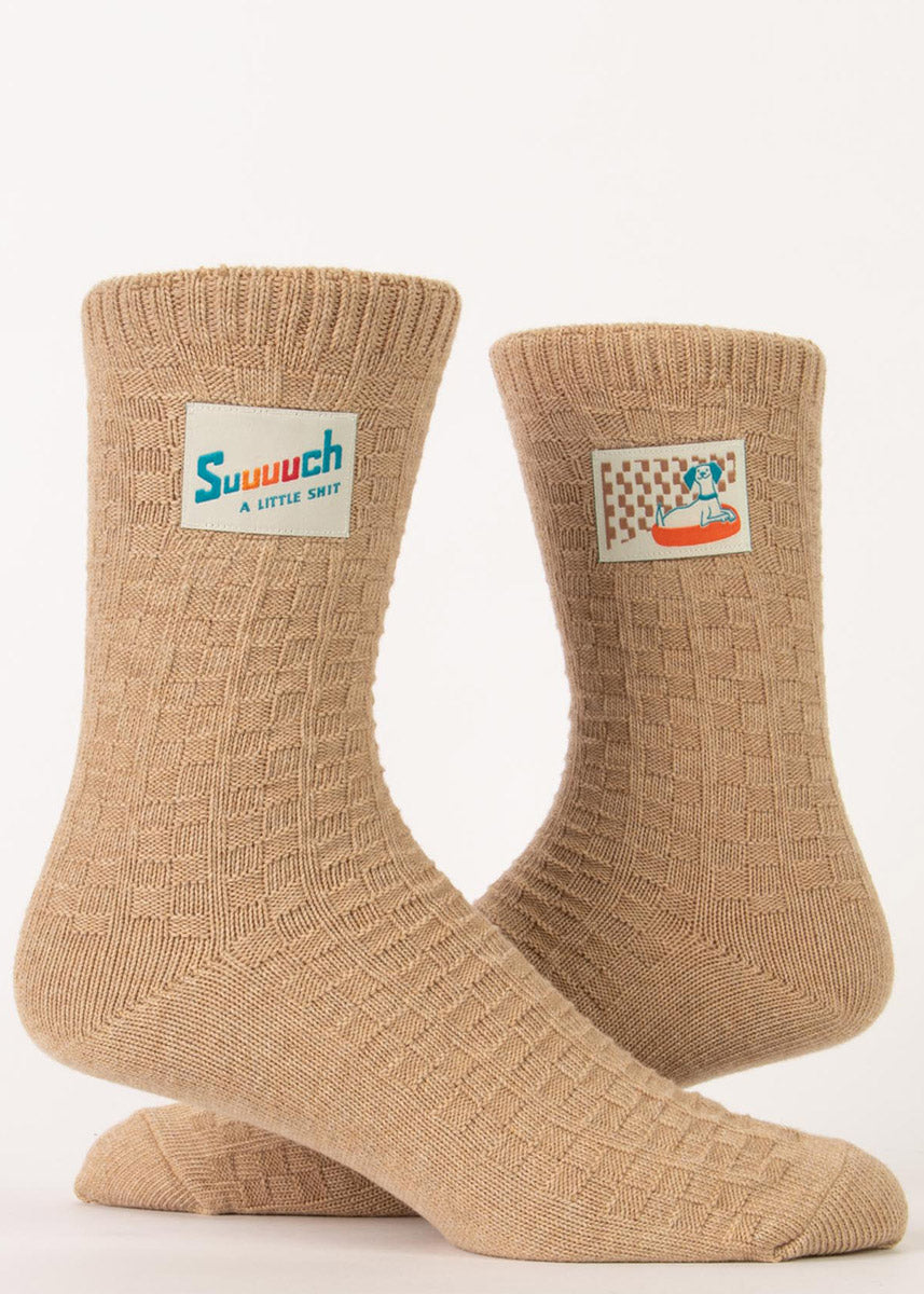 Funny dog socks feature tags that show a cute pup and say &quot;Suuuuch a little shit&quot; on a beige knit background made of organic cotton.