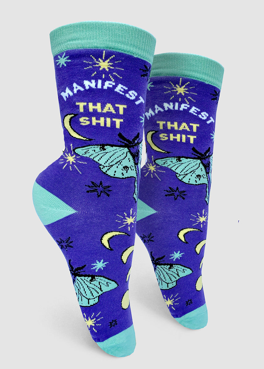 Funny swear-word socks for women feature crescent moons and luna moths on an indigo background with the words, "Manifest that shit."