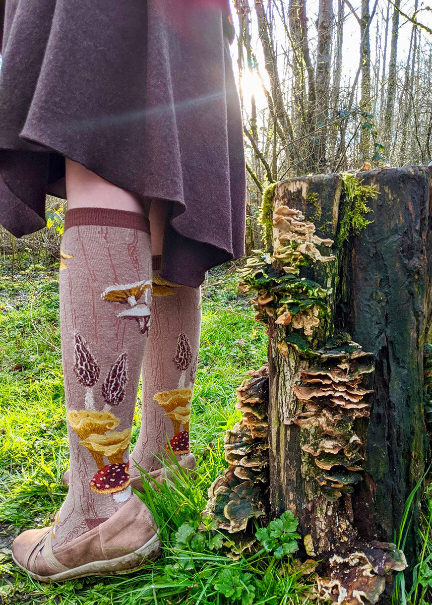Mushroom knee socks feature a variety of realistic fungi growing on a wood-grain background.
