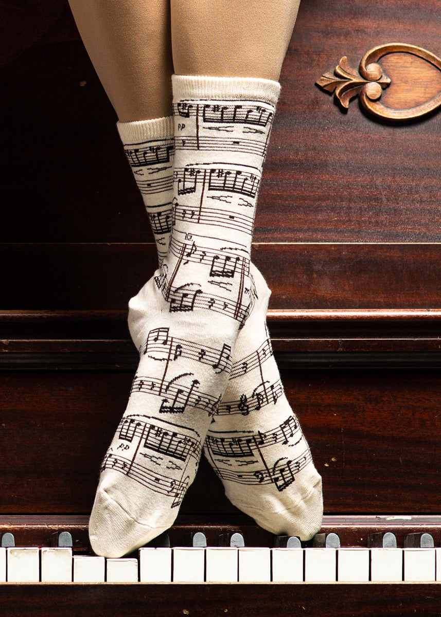 Novelty music note socks that compose Beethoven&#39;s &quot;Fur Elise&quot; are worn by a model posed with her feet on a piano&#39;s keys.