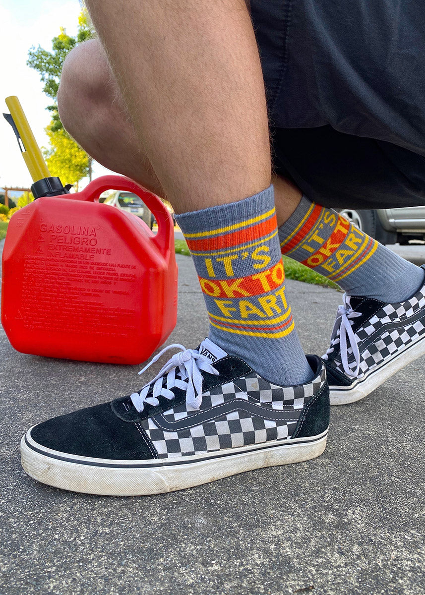Funny socks for men say &quot;It&#39;s OK to fart&quot; and feature retro stripes on a gray background.