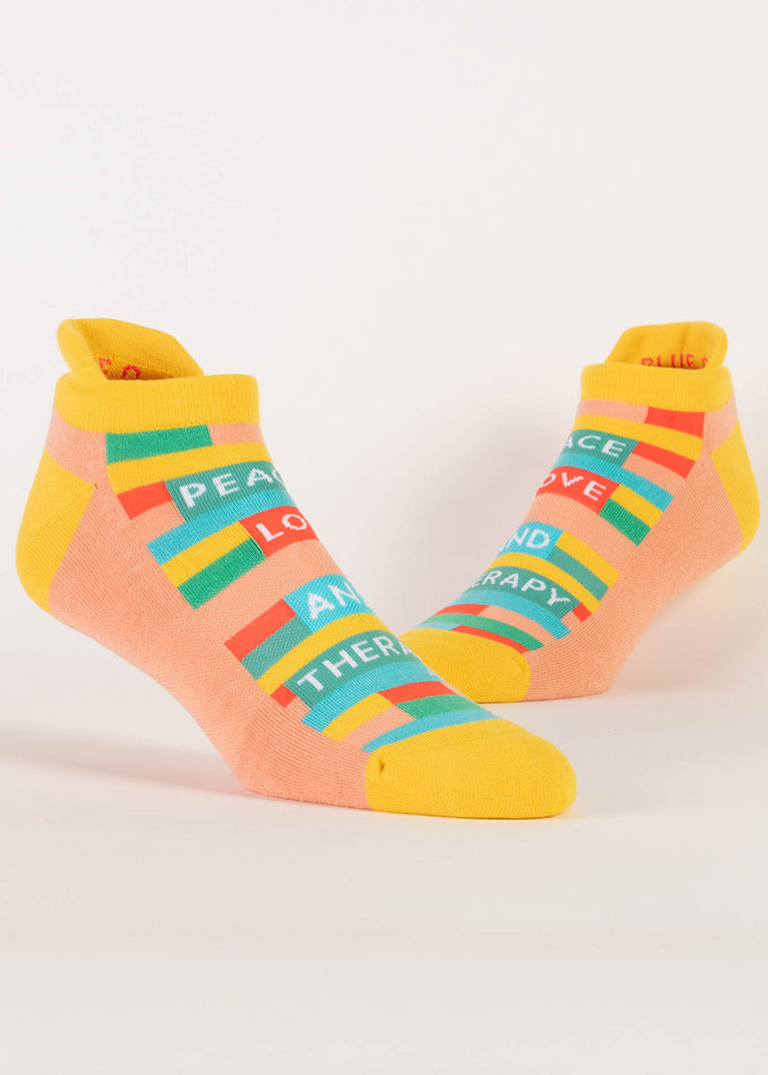 Striped orange, yellow and aqua athletic ankle socks with a message of “Peace, Love and Therapy” on the foot.