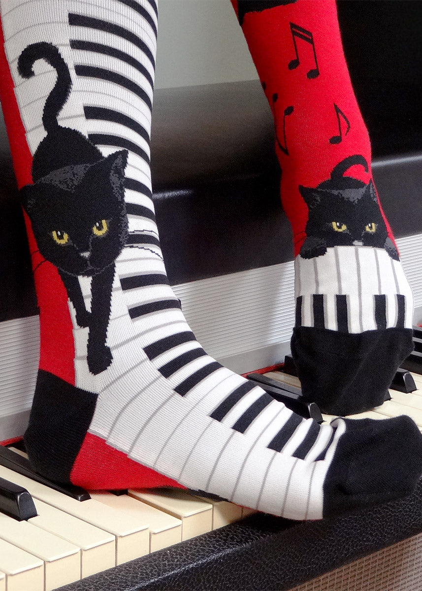 Knee-high cat socks show adorable black cats prancing on ivory piano keys!
